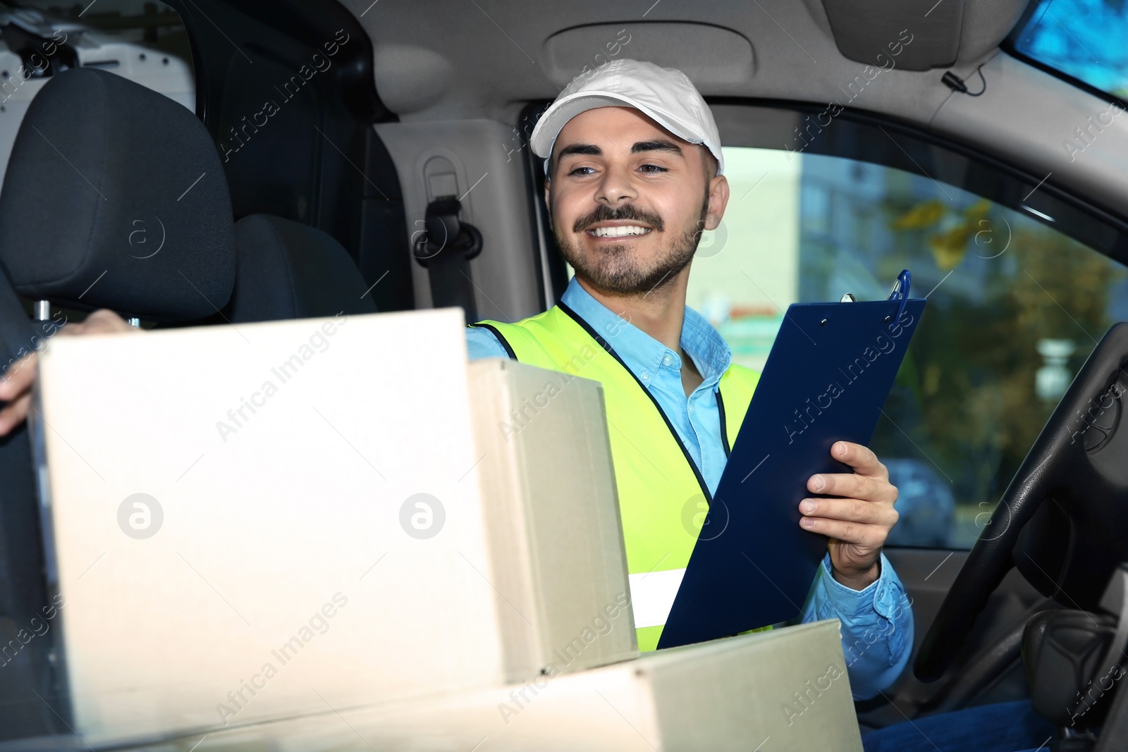 Photo of Young courier checking amount of parcels in delivery van