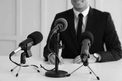 Image of Journalist conference. Businessman giving interview at table with microphones indoors, closeup. Black and white effect