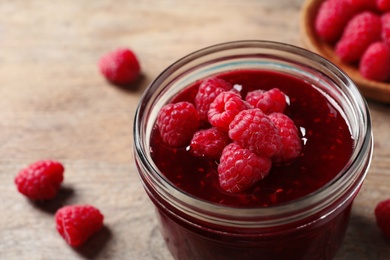 Glass jar of sweet jam with ripe raspberries on wooden table, closeup