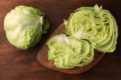 Photo of Fresh green cut and whole iceberg lettuce heads on wooden table, flat lay