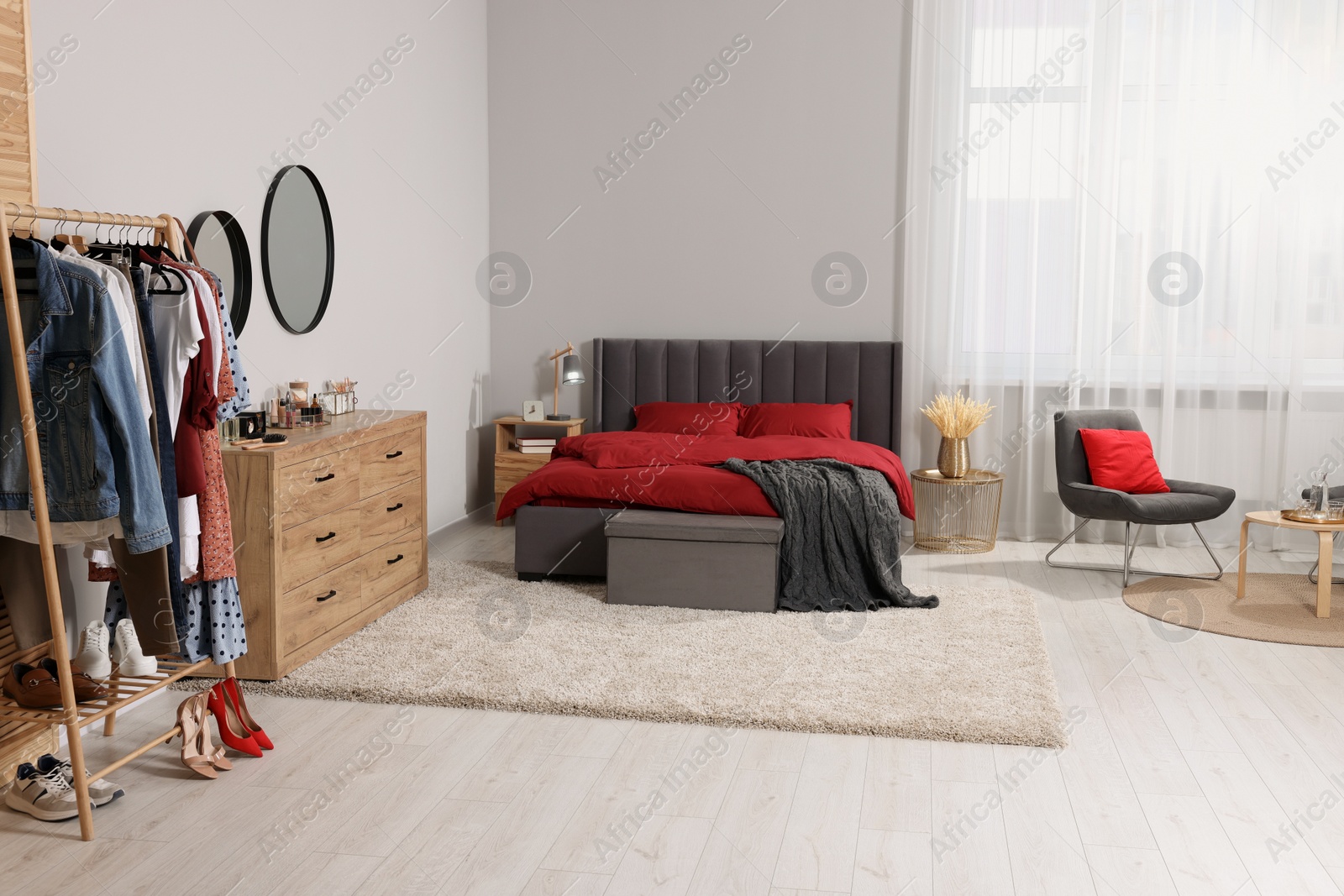 Photo of Stylish bedroom with comfortable bed, armchair, table, wooden chest of drawers and clothing rack. Interior design