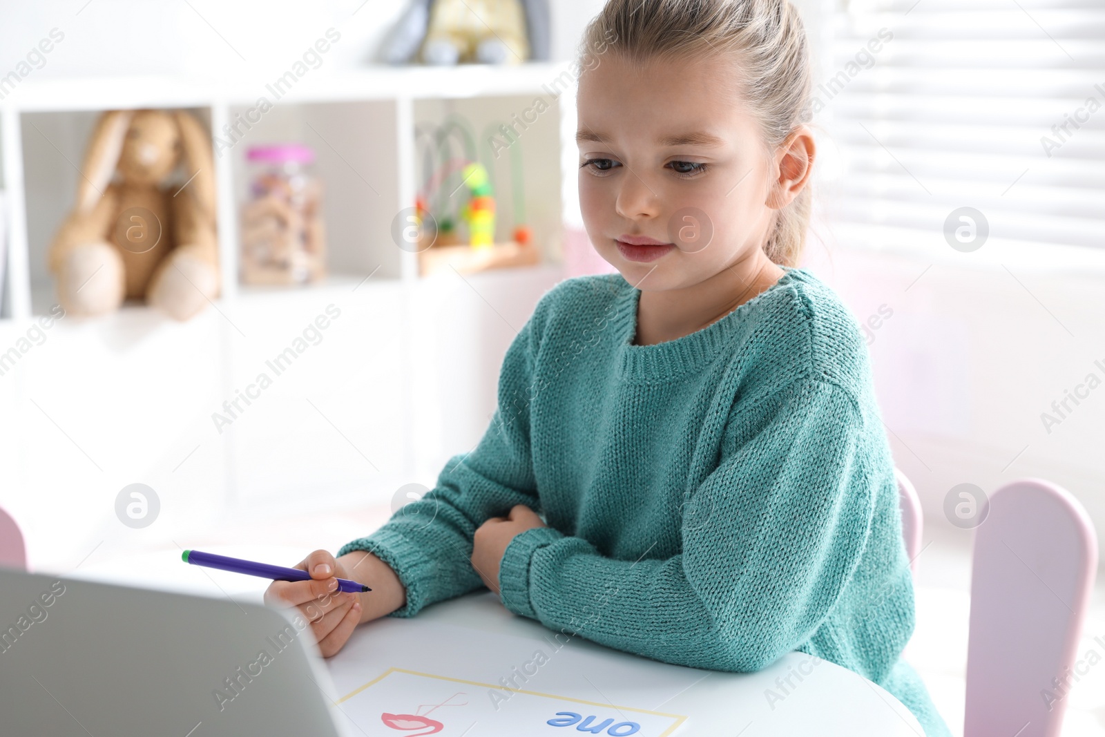 Photo of Little girl learning English indoors at online lesson