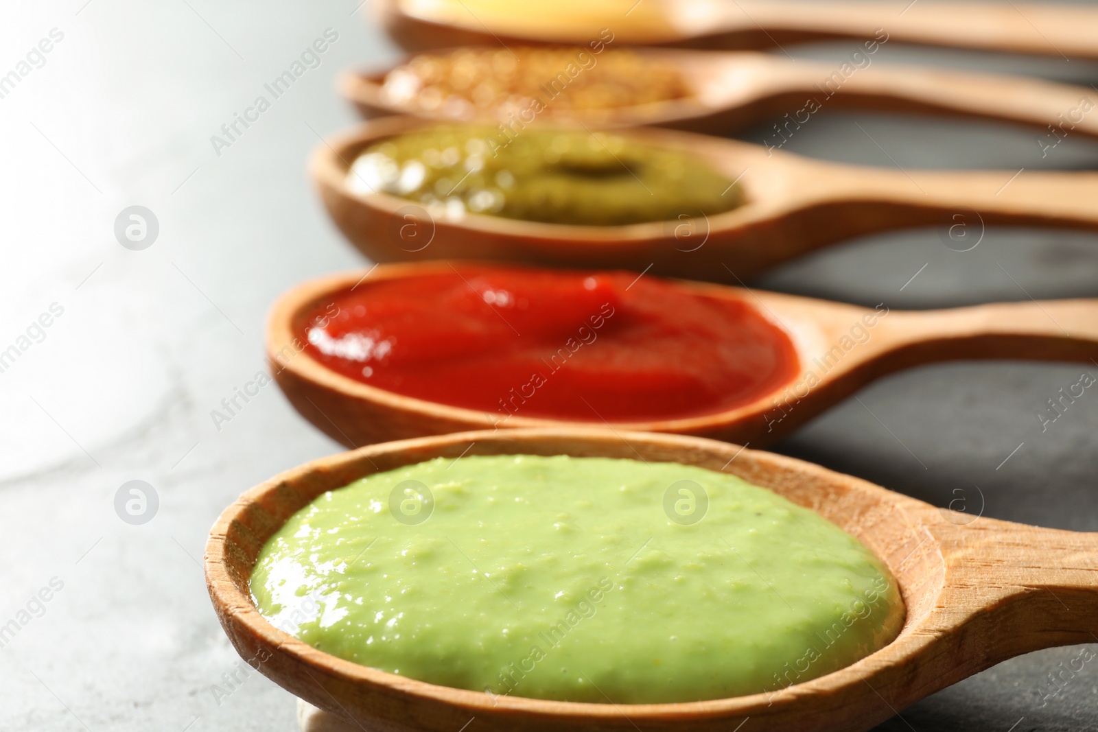 Photo of Set of wooden spoons with different delicious sauces on grey table, closeup