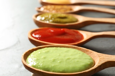 Photo of Set of wooden spoons with different delicious sauces on grey table, closeup