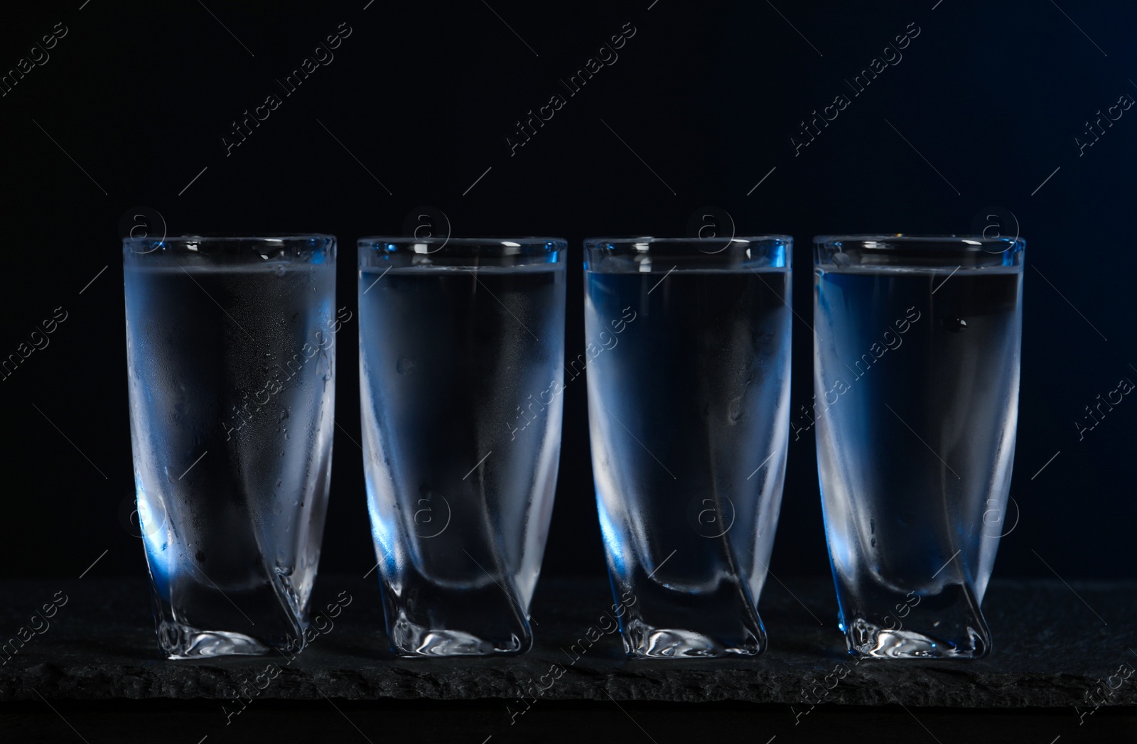 Photo of Set of glasses with vodka on black table, closeup