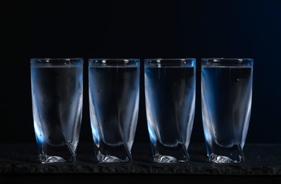 Photo of Set of glasses with vodka on black table, closeup