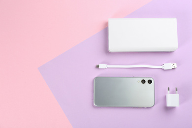 Mobile phone, portable charger and cable on color background, flat lay. Space for text