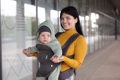 Mother holding her child in sling (baby carrier) near building outdoors