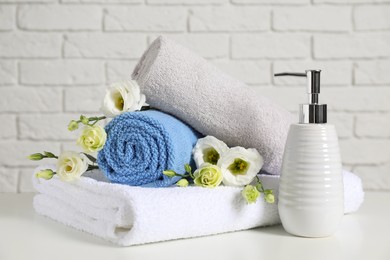 Photo of Clean soft towels with flowers and soap dispenser on table near white brick wall