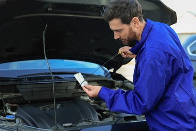 Photo of Worker checking motor oil level with dipstick outdoors