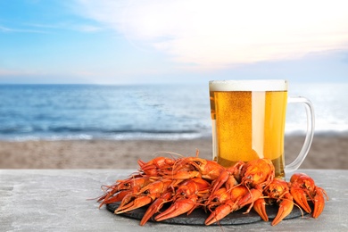 Image of Cooked crayfishes served with beer on grey table near sea