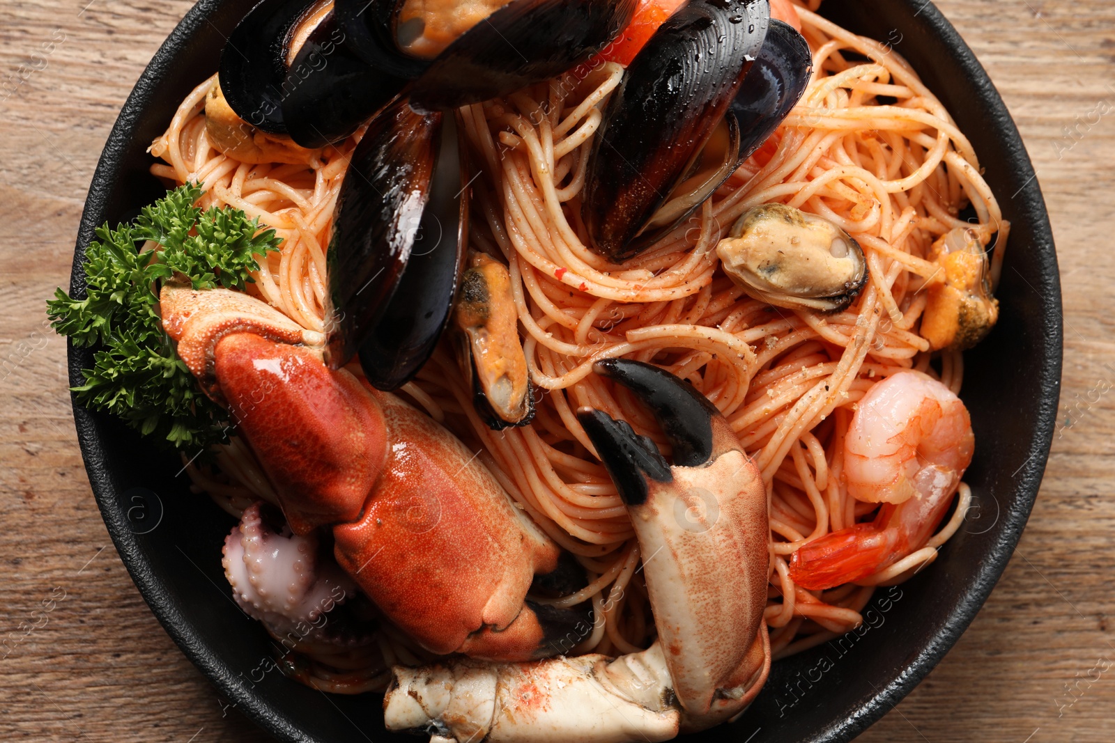 Photo of Delicious spaghetti with seafood served on wooden table, top view