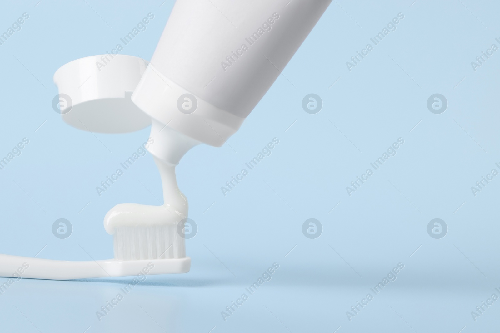 Photo of Applying paste on toothbrush against light blue background, space for text