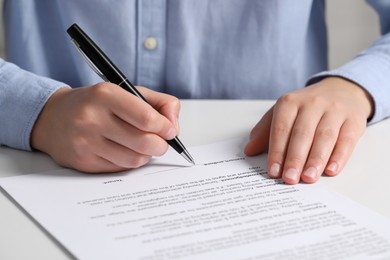 Photo of Woman signing document at white table, closeup