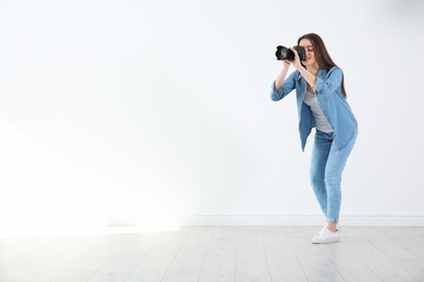 Female photographer with camera near light wall indoors