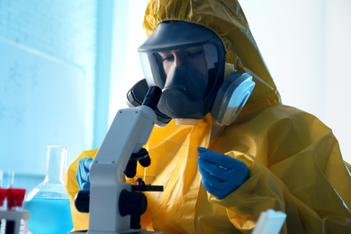 Scientist in chemical protective suit using microscope at laboratory. Virus research