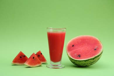 Glass of delicious drink and cut fresh watermelon on light green background