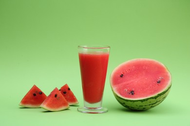 Photo of Glass of delicious drink and cut fresh watermelon on light green background