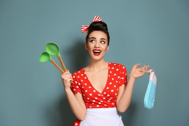 Funny young housewife with oven mitten and cooking utensils on color background