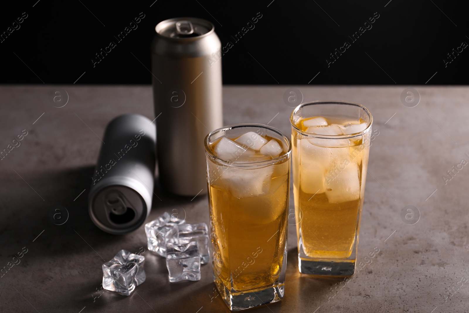 Photo of Energy drink in glasses, aluminium cans and ice cubes on grey table