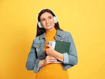 Young woman listening to audiobook on yellow background