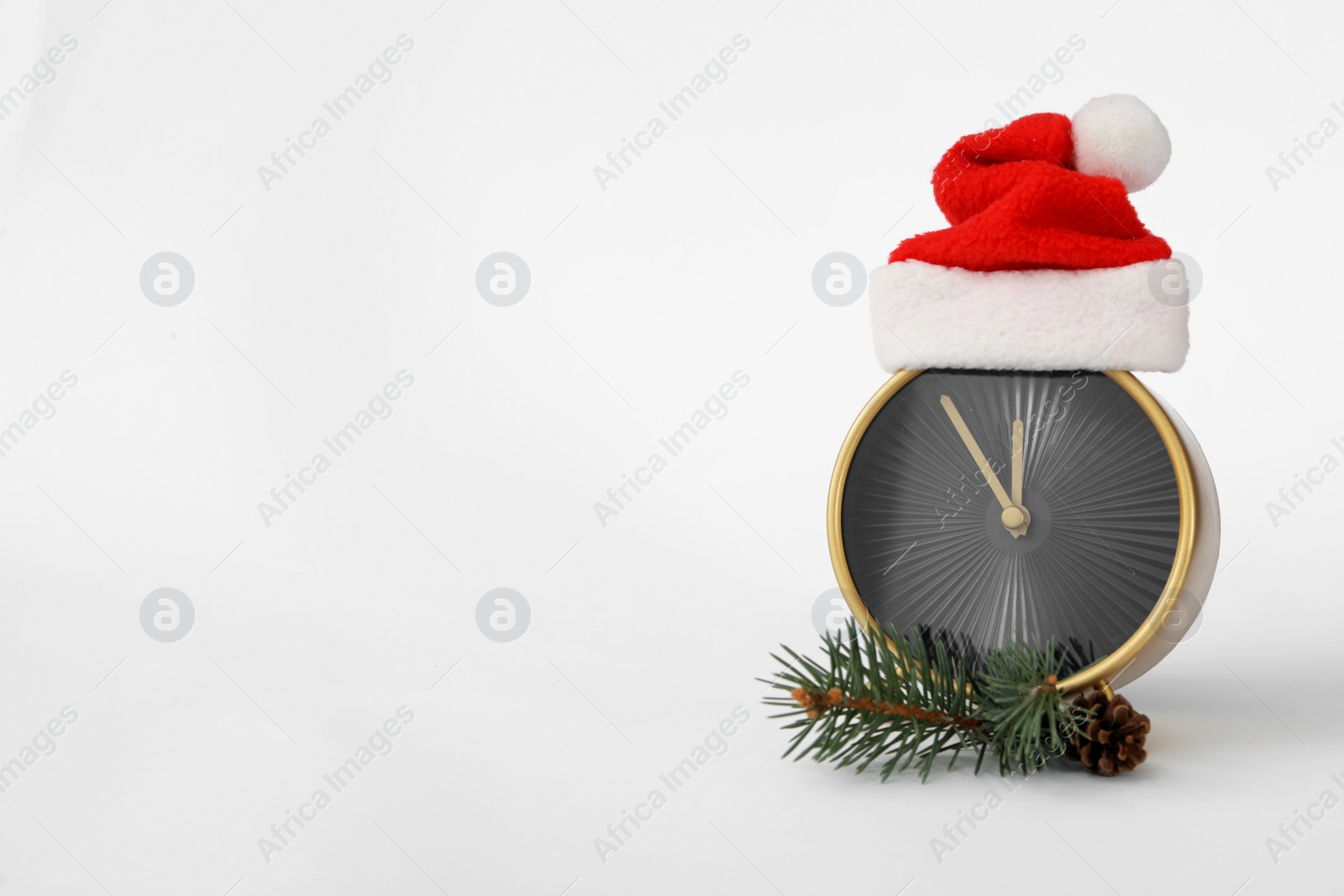 Photo of Alarm clock in Santa hat and fir branch on white background, space for text. New Year countdown