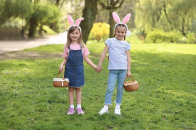Easter celebration. Cute little girls with bunny ears holding wicker baskets outdoors