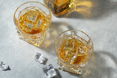 Whiskey in glasses with ice cubes on grey textured table, above view