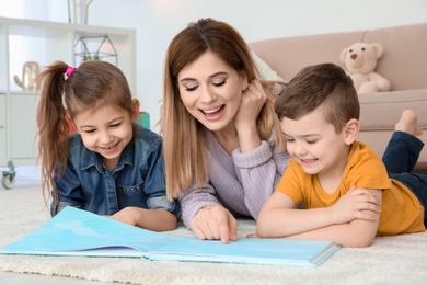 Photo of Little children with their nanny lying on floor and reading book at home