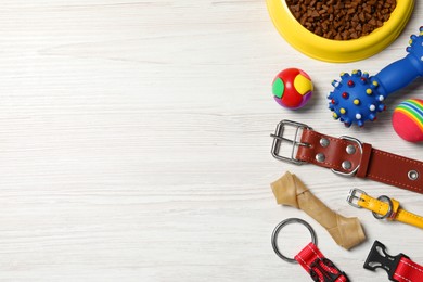 Photo of Flat lay composition with dog collars, toys and food on white wooden table. Space for text