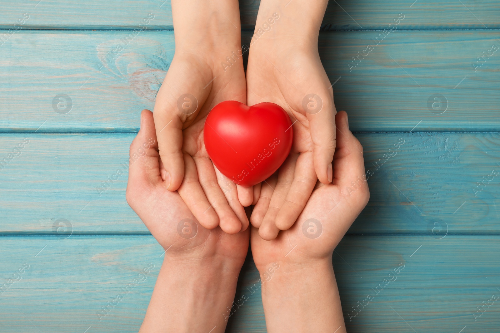 Photo of Couple holding red heart in hands at light blue wooden table, top view