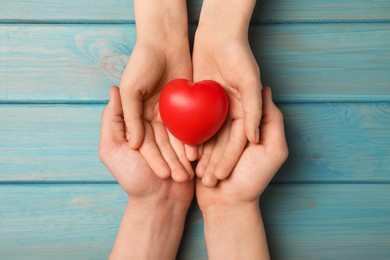 Couple holding red heart in hands at light blue wooden table, top view