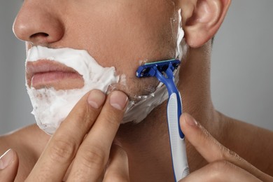 Photo of Man shaving with razor on grey background, closeup