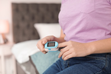 Young woman checking pulse with digital medical device indoors, closeup. Space for text