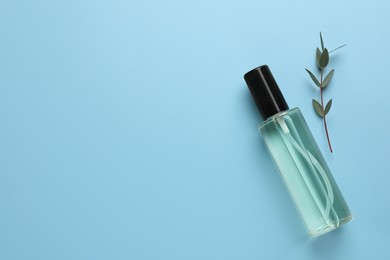 Photo of Bottle of baby oil and leaves on light blue background, flat lay. Space for text