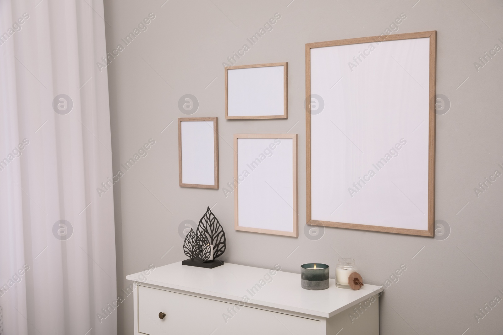 Photo of Empty frames hanging on grey wall over white chest of drawers. Mockup for design