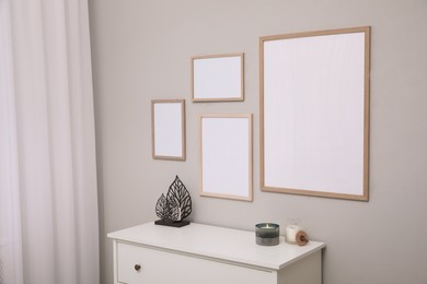 Empty frames hanging on grey wall over white chest of drawers. Mockup for design