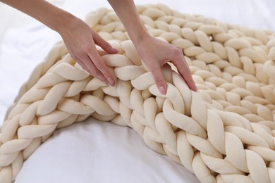 Photo of Woman folding chunky knit blanket on bed at home, closeup