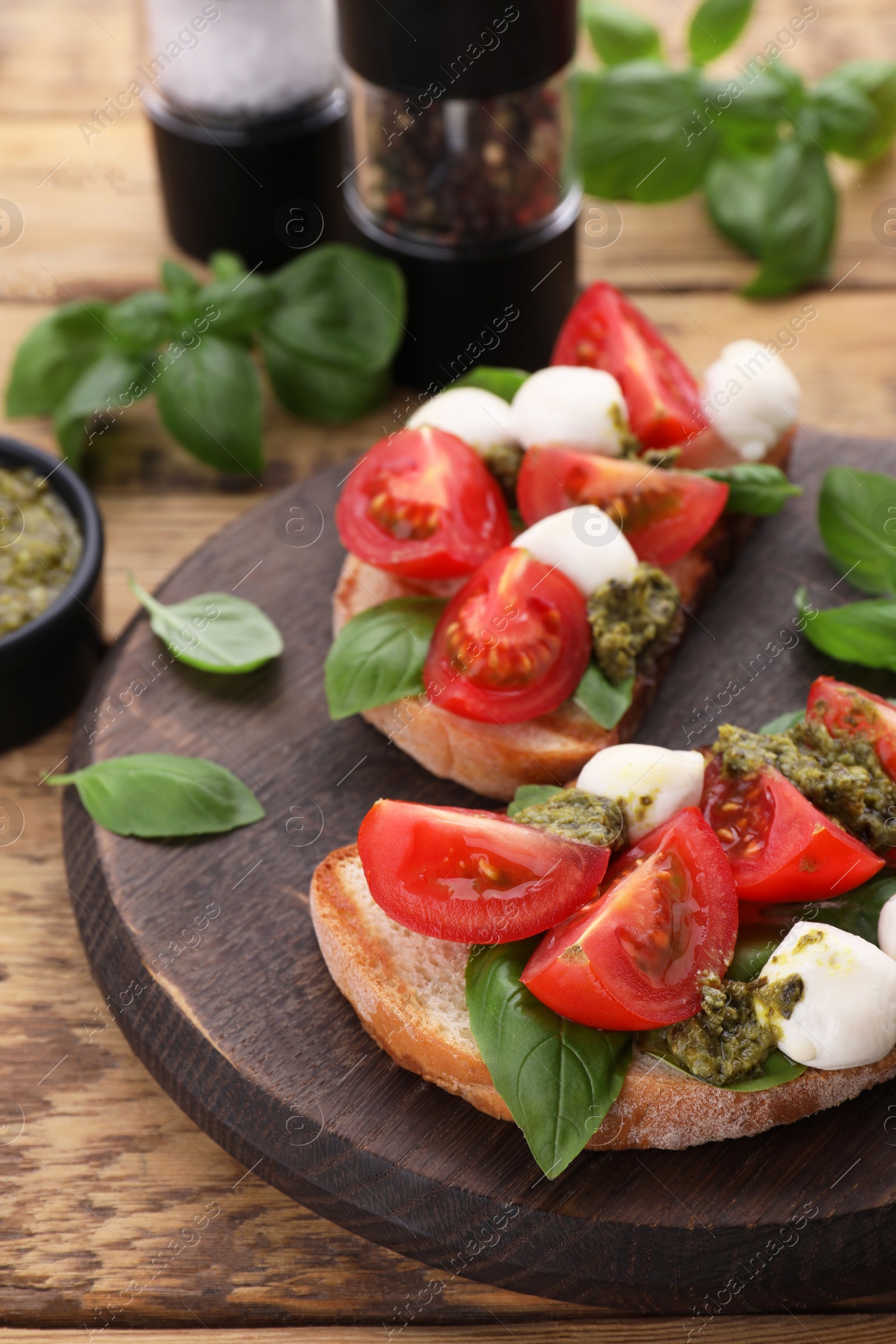 Photo of Delicious Caprese sandwiches with mozzarella, tomatoes, basil and pesto sauce on wooden table, closeup