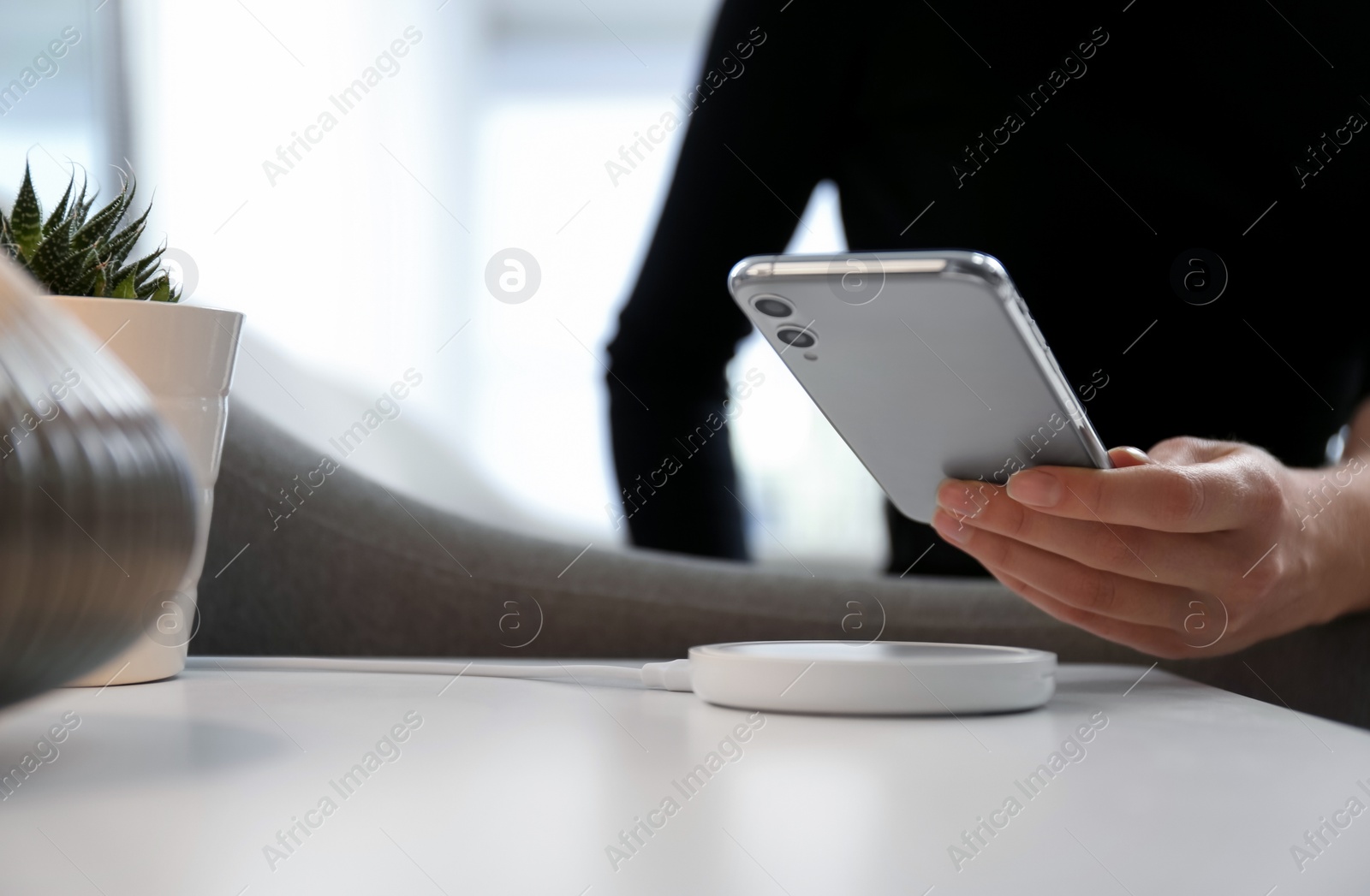 Photo of Woman putting smartphone on wireless charger in room, closeup. Space for text