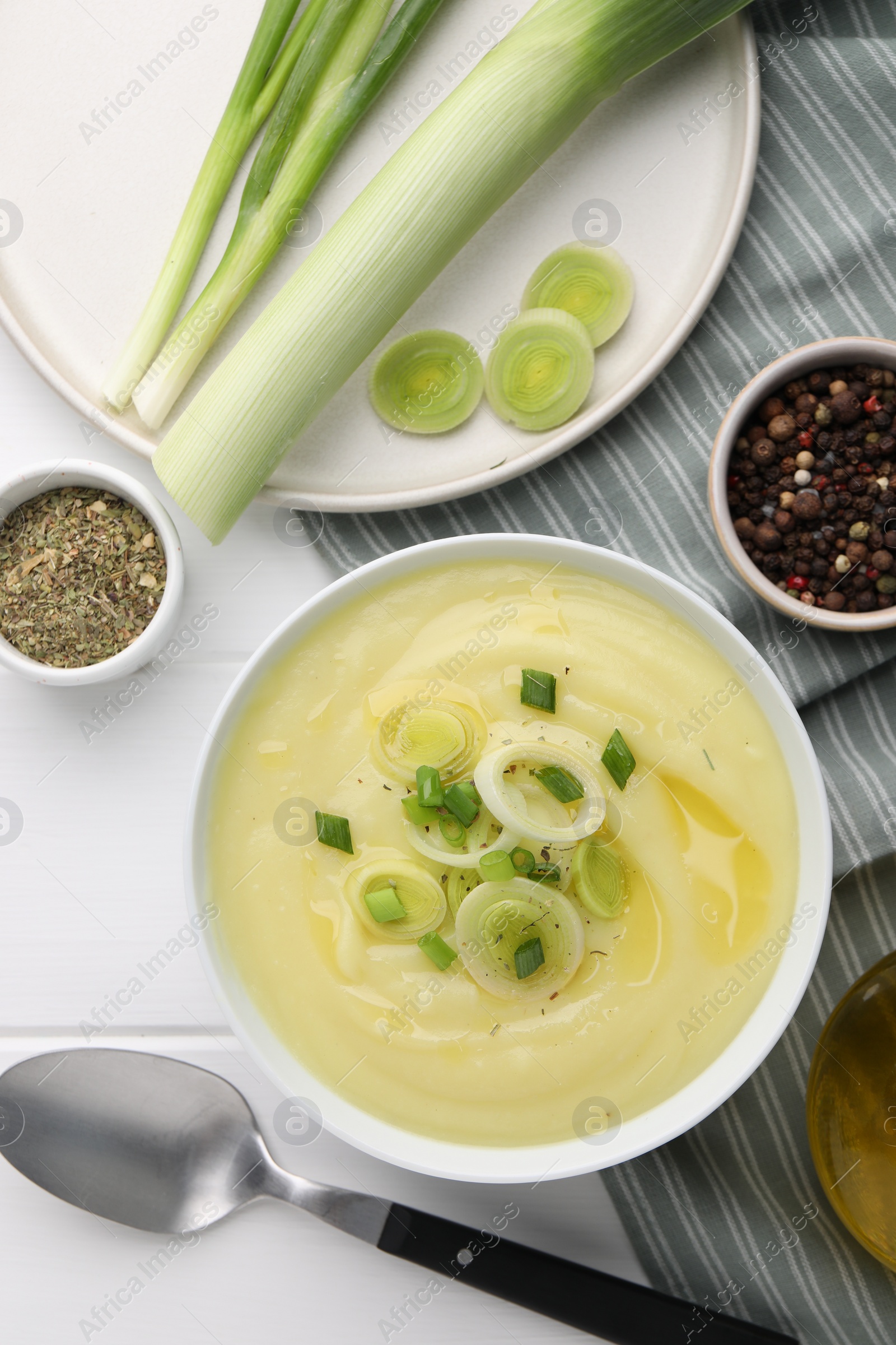 Photo of Bowl of tasty cream soup with leek and spoon on white wooden table, flat lay