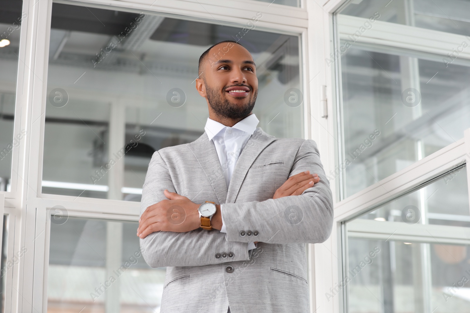 Photo of Happy man with crossed arms in office, low angle view. Lawyer, businessman, accountant or manager