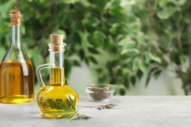 Photo of Hemp oil and leaves on grey table against blurred background. Space for text