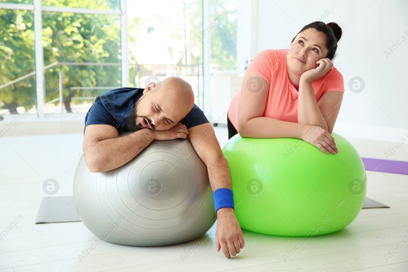 Photo of Tired overweight man and woman resting on fitness balls in gym