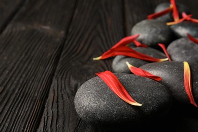 Photo of Spa stones and flower petals on wooden table, closeup. Space for text