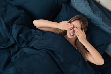 Photo of Young woman waking up in comfortable bed with dark blue linens, above view