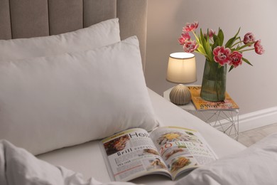 Photo of Stylish lamp, flowers and magazine on bedside table indoors. Bedroom interior elements