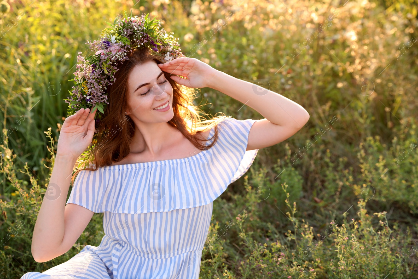 Photo of Young woman wearing wreath made of beautiful flowers outdoors on sunny day