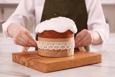 Photo of Woman wrapping delicious Easter cake with ribbon at white marble table in kitchen, closeup