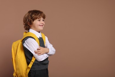 Happy schoolboy with backpack on brown background, space for text